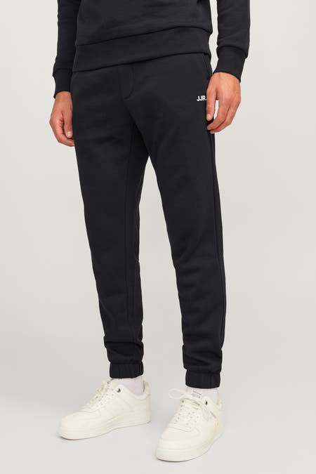 Zwarte jogging van JJREBEL, met een wit logo, gecombineerd met witte sneakers en sokken.