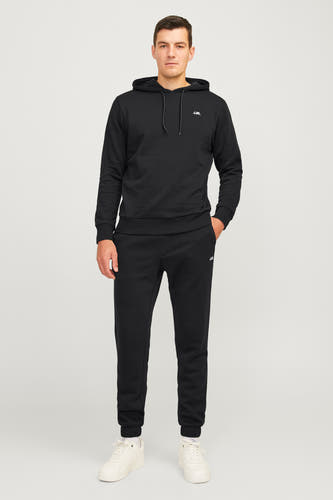 Zwarte jogging van JJREBEL, gecombineerd met een zwarte hoodie, witte sokken en crèmekleurige sneakers.