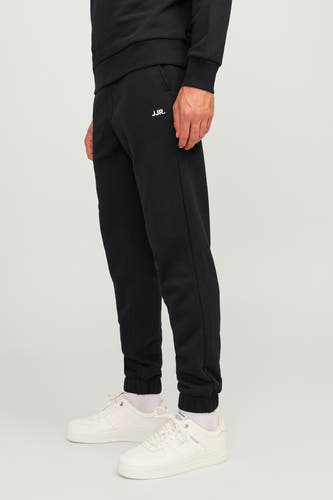 Zwarte joggingbroek van JJREBEL, met het logo op de broekspijp en witte sneakers.
