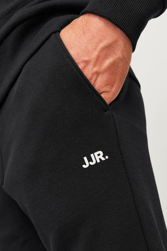 Zwarte joggingbroek van JJREBEL, met een hand in de zak en witte merkletters.