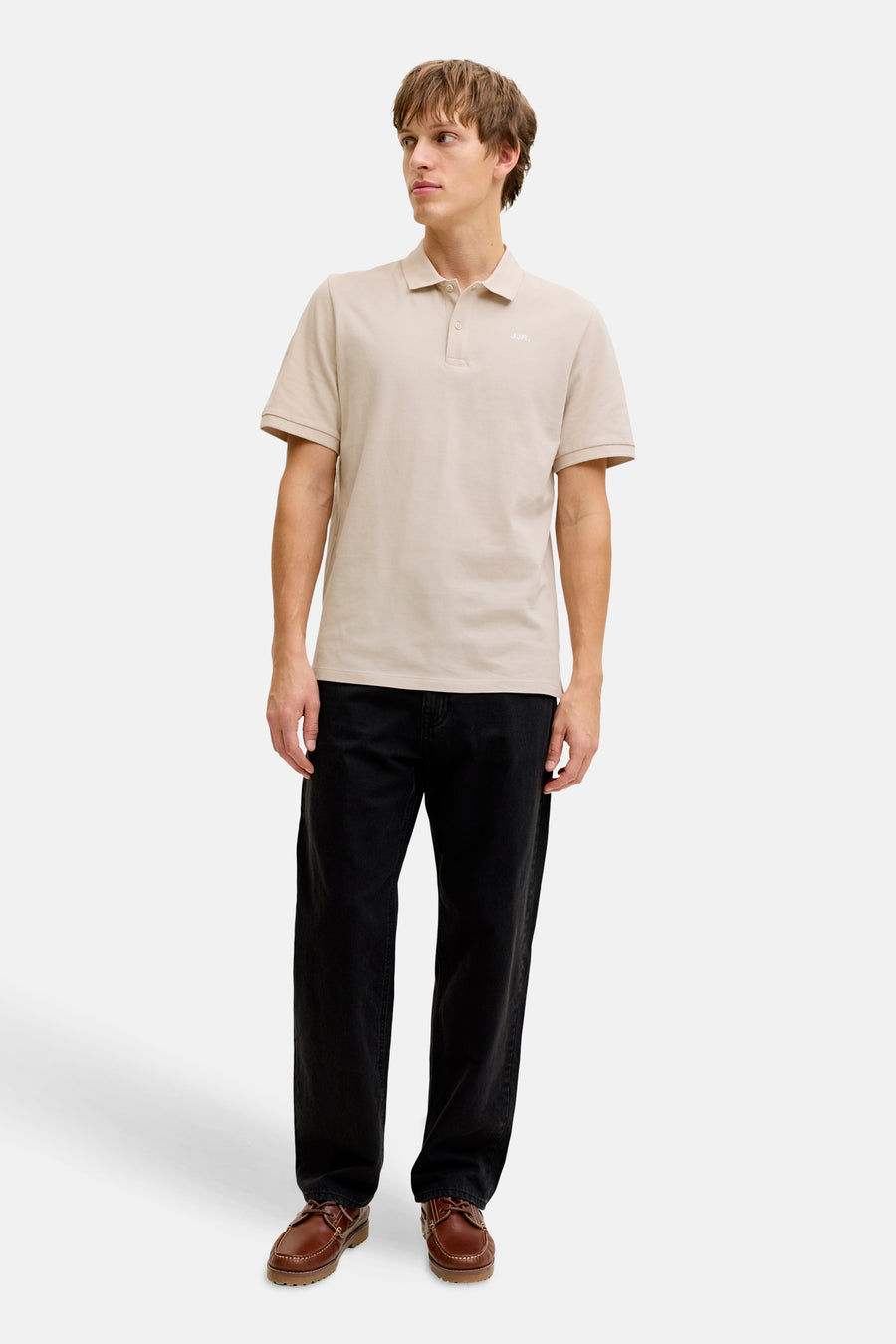 Beige polo van JJREBEL, met korte mouwen, gedragen met een zwarte broek en bruine schoenen.
