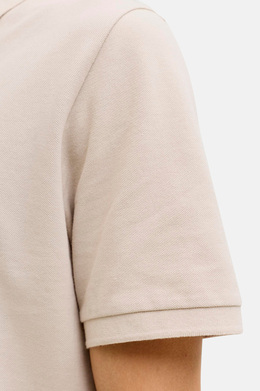 Beige polo van JJREBEL, close-up van de mouw met geribbelde boord en subtiele textuur.
