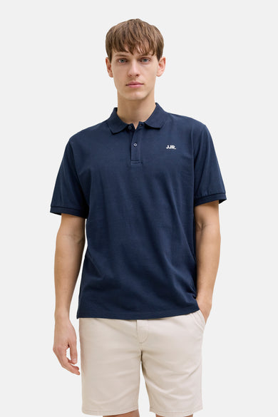 Polo bleue de JJREBEL, à manches courtes et portée avec un short beige et des sandales marron.