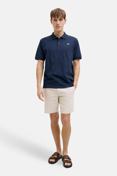 Blauwe polo van JJREBEL, met korte mouwen en gedragen met beige shorts en bruine sandalen.
