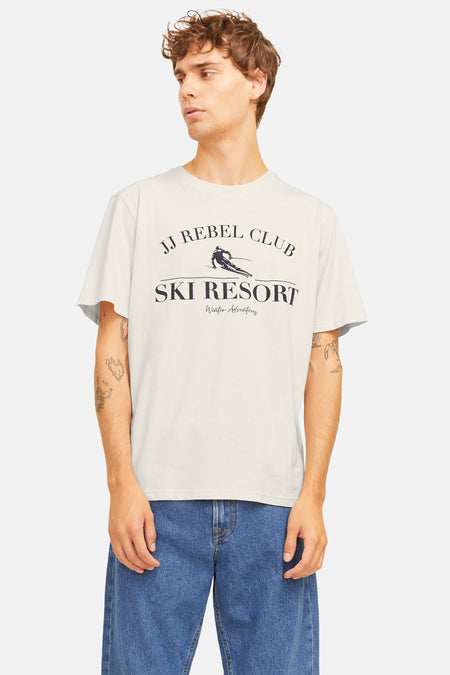Beige T-shirt met korte mouwen van JJREBEL, met opdruk van ski resort en gedragen met een blauwe jeans.
