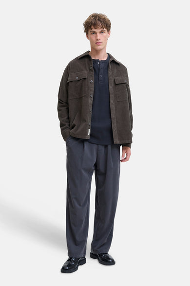 T-shirt bleu marine à manches longues de PREMIUM BLUE par JACK & JONES, porté sous un gilet corduroy marron avec un pantalon gris et des chaussures noires.