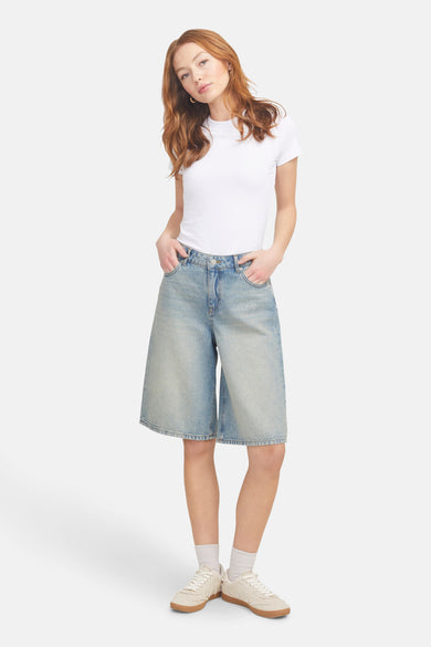 Short de denim bleu clair court de JJXX, porté avec un T-shirt blanc, des chaussettes blanches et des baskets crème.
