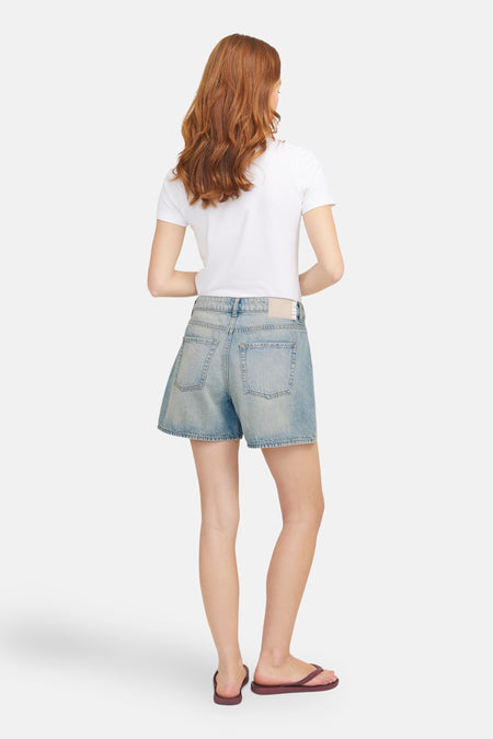 Short en denim bleu clair de JJXX, vu de de derrière, associé à un T-shirt blanc et des chaussons rouges.