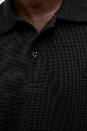 Zwarte polo met korte mouwen van CORE BY JACK & JONES, met een subtiele wafeltextuur en een knoopsluiting.
