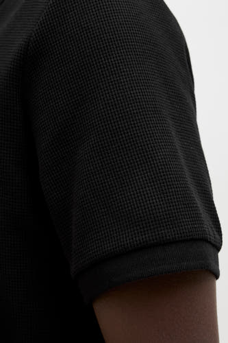 Zwarte polo met korte mouwen van CORE BY JACK & JONES, met een wafelstructuur en een donkere huidskleur.