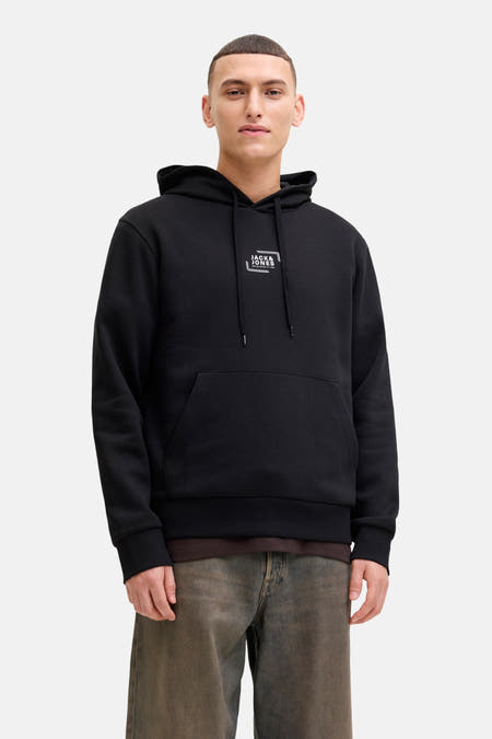 Zwarte sweater met kap van CORE by JACK & JONES, met trekkoorden en buidelzak, gedragen met een bruin shirt en een jeansbroek.
