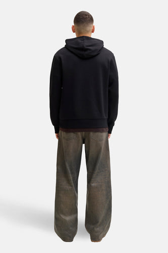 Achterkant van een man met een zwarte hoodie en brede, bruine jeans.