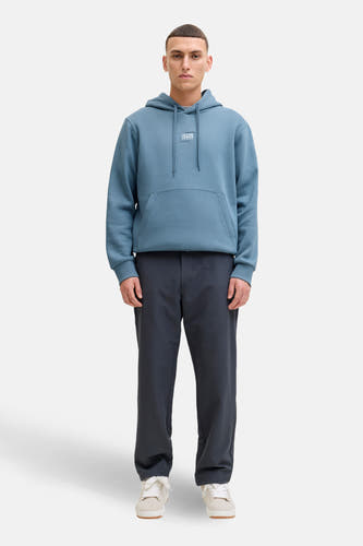 Blauwe sweater met kap van CORE by JACK & JONES, met lange mouwen en kangoeroezak, gecombineerd met donkere broek en witte sneakers.