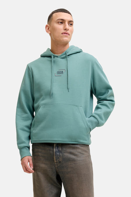Pull-over bleu avec capuche de CORE BY JACK & JONES, avec cordon de serrage, une poche et porté avec un pantalon et des chaussures.