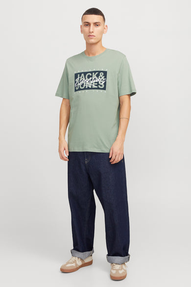 T-shirt vert de mantes man manmanSSSSSS & J J J J d d logo, combiné avec des jeans foncés et des baskets beige.