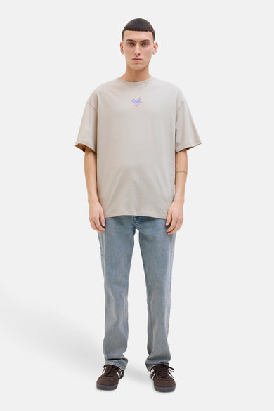 Beige T-shirt met korte mouwen van ORIGINALS BY JACK & JONES, met klein logo op de borst, gedragen met jeans en sneakers.
