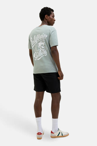 T-shirt vert de mantes courtes man ORIGINALSSSS J &, avec une imprimé "California Surfing" sur le dos, porté avec des short noirs.