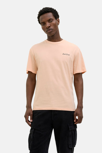 T-shirt orange à manches courtes d'ORIGINALS BY JACK & JONES, avec un petit texte noir, associé à un pantalon noir et des baskets blanches.