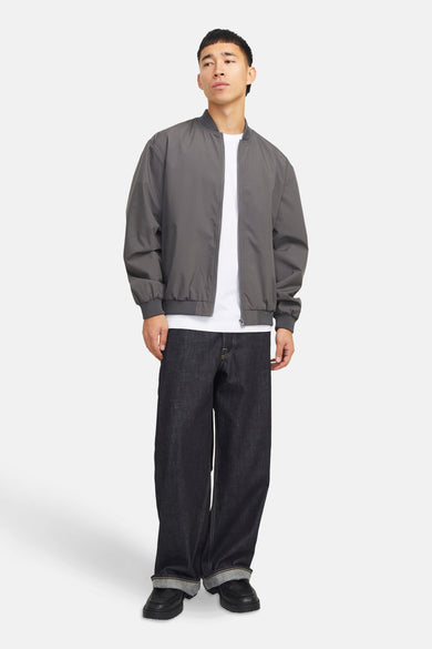 Korte grijze jas van PREMIUM by JACK & JONES, gedragen over een wit T-shirt met wijde donkere jeans en zwarte schoenen.