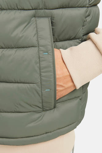 Kaki bodywarmer van PREMIUM BLUE by JACK & JONES, met hand in zak en een beige trui.
