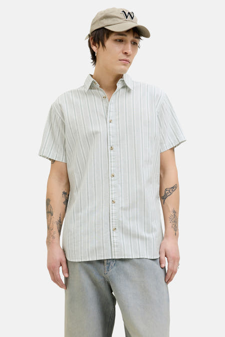 Chemise rayée verte de PREMIUM BLUE par JACK & JONES, à manches courtes, portée avec un chapeau et des jeans larges.