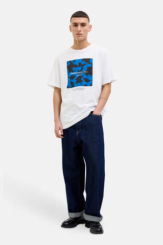 Wit T-shirt met korte mouwen van CORE BY JACK & JONES, met blauw en zwart patroon op de borst, gedragen met donkerblauwe jeans en zwarte schoenen.