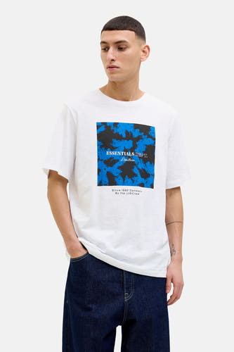 Wit T-shirt met korte mouwen van CORE BY JACK & JONES, met blauw-zwart patroon op de voorkant, gedragen met donkere jeans.
