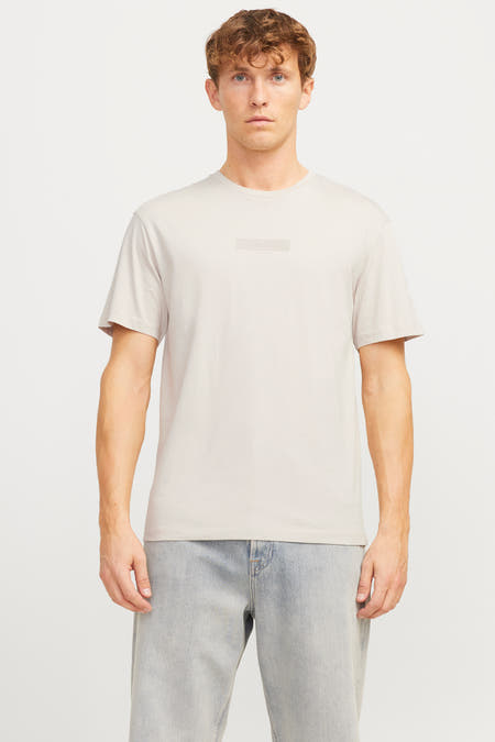 Ecru T-shirt met korte mouwen van CORE BY JACK & JONES, met een subtiel logo op de borst en gedragen met blauwe jeans.
