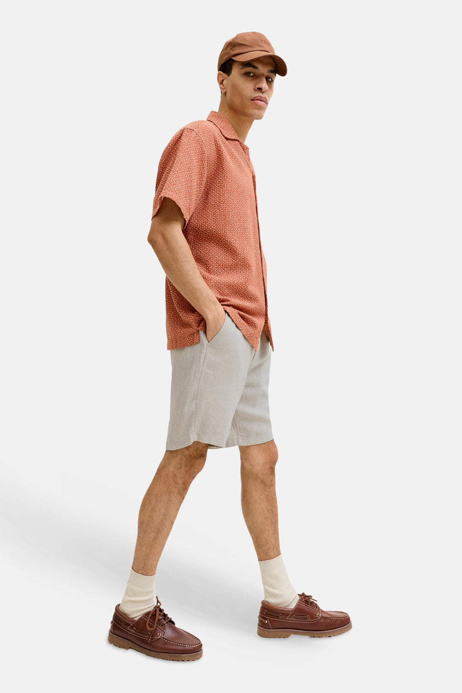 Beige short van JACK & JONES JEANS INTELLIGENCE met subtiele textuur, gedragen door een man met oranje overhemd en bruine schoenen.