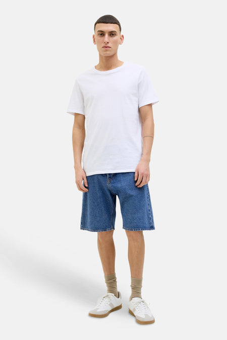 Mid blauwe denim jeansshort van JACK & JONES JEANS INTELLIGENCE met wijde pasvorm, gestyled met een wit T-shirt, beige sokken en witte sneakers.