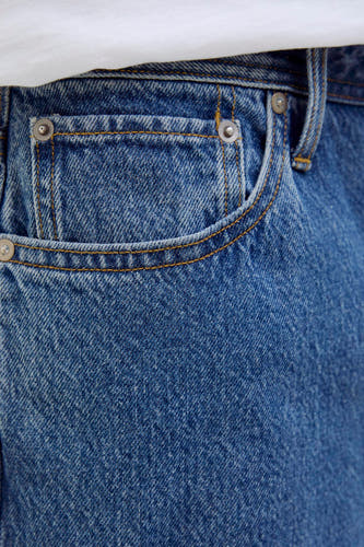 Short en jean bleu moyen de JACK & JONES JEANS INTELLIGENCE, gros plan de la poche avec surpiqûres orange, rivets métalliques et t-shirt blanc.