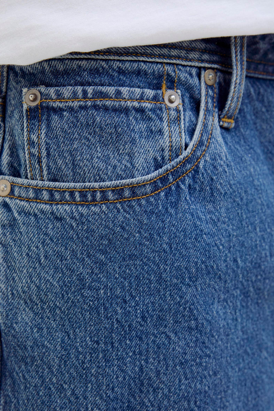 Short en jean bleu moyen de JACK & JONES JEANS INTELLIGENCE, gros plan de la poche avec surpiqûres orange, rivets métalliques et t-shirt blanc.