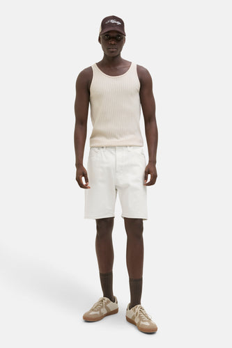 Staande man in hemdje, witte korte broek, bruine sokken, en bruine sneakers.