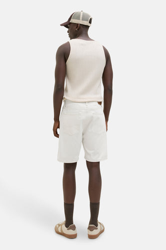 Man van achteren in een mouwloze top, witte korte broek en sneakers.