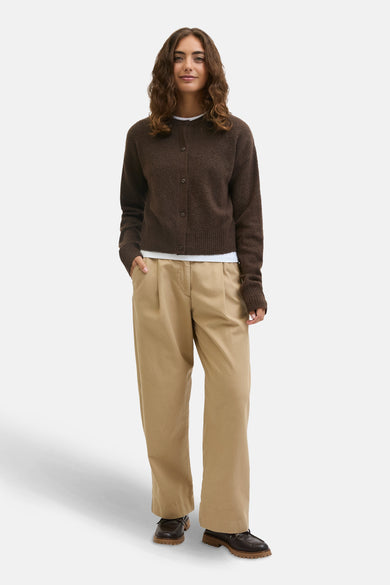 Bruin vest van JJXX, gedragen over een wit shirt, met beige plooibroek en donkerbruine schoenen.
