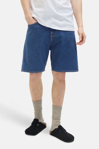 Short en jean JJREBEL, en denim bleu moyen, porté avec un t-shirt blanc, des chaussettes grises et des mules noires.