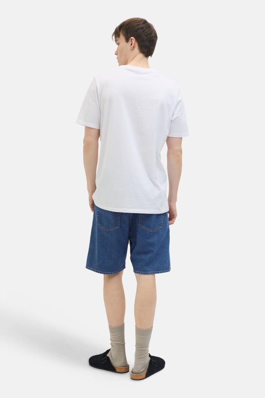 Short en jean en denim bleu moyen de JJREBEL, avec poches arrière et porté avec un T-shirt blanc, des chaussettes et des mules.