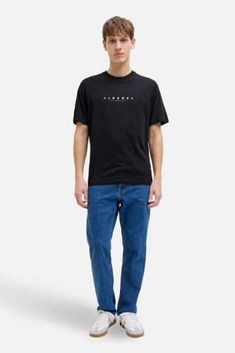 Zwart T-shirt met korte mouwen van JJREBEL, gedragen met blauwe jeans en witte sneakers.