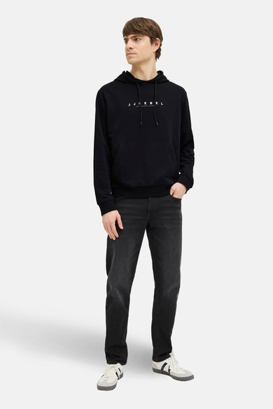 Zwarte sweater met kap van JJREBEL, gedragen met een donkere jeans en witte sneakers.