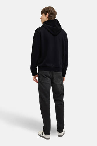 Zwarte sweater met kap van JJREBEL, gezien van achteren, gecombineerd met donkere jeans en lage sneakers.