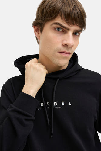 Zwarte sweater met kap van JJREBEL, met witte "REBEL" letters op de borst, gedragen door een man.
