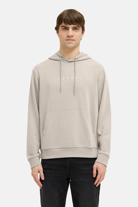 Pull beige à capuche JJREBEL, avec poche kangourou et jean noir.