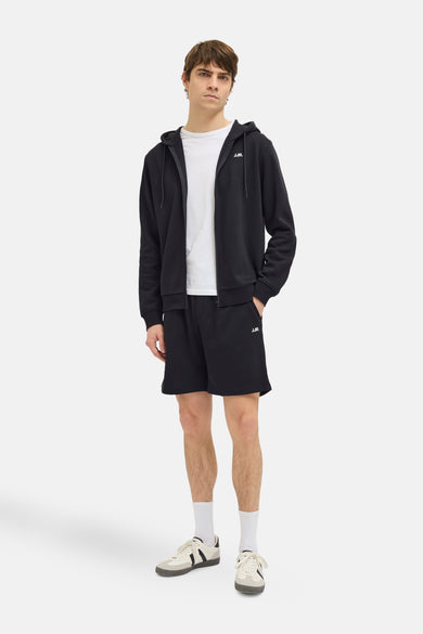 Zwarte short van JJREBEL, gedragen met een wit T-shirt, zwarte hoodie en witte sokken met sneakers.