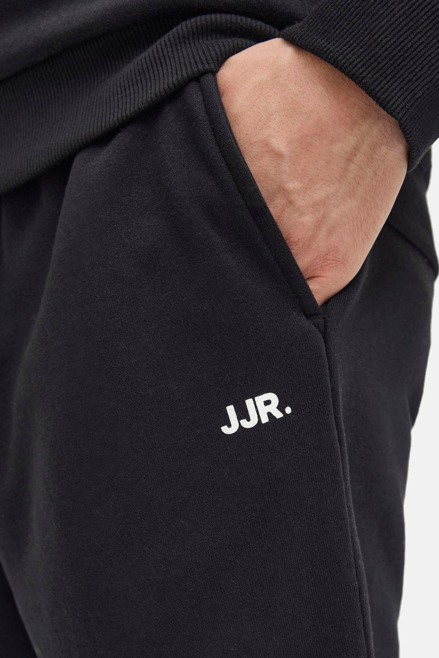 Short noir de JJREBEL, avec une main dans la poche et le logo JJR. sur la pipe.