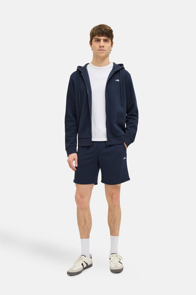 Donkerblauwe short van JJREBEL, gecombineerd met een wit T-shirt, een donkerblauw vest met ritssluiting, witte sokken en sneakers.