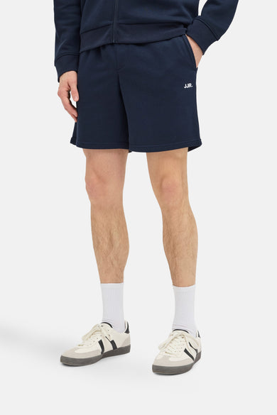 Donkerblauwe short van JJREBEL, met witte logo-opdruk, gedragen met witte sokken en crèmekleurige sneakers.
