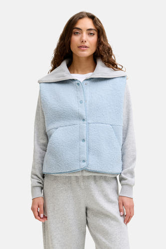 Gilet bodywarmer bleu de JJXX, avec fermeture à boutons et texture polaire, porté sur un pull gris et un pantalon de jogging.