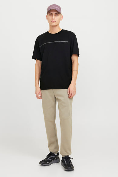 Zwart T-shirt met korte mouwen van CORE by JACK & JONES, met een horizontale streep op de borst, gecombineerd met beige joggingbroek en zwarte sneakers.
