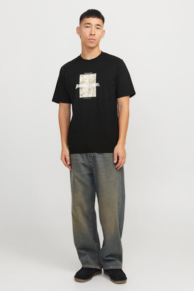 T-shirt noir à manches courtes d'ORIGINALS BY JACK & JONES, avec une impression graphique sur la partie avant, associé à des jeans bleus et des chaussures noires.