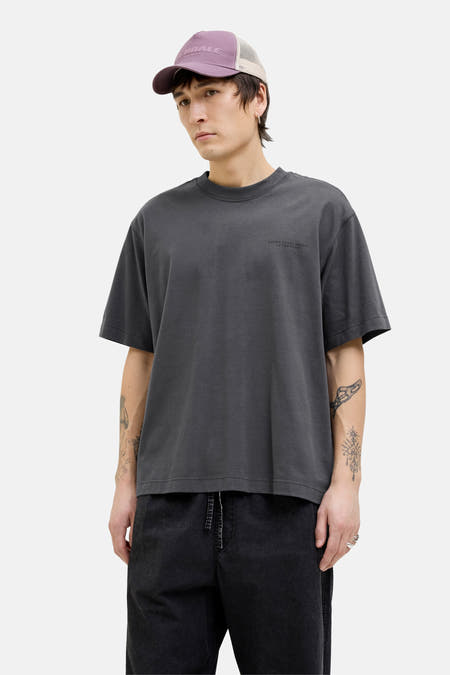 Grijs T-shirt met korte mouwen van CORE BY JACK & JONES, met tekst op de borst, gedragen met een pet en zwarte broek.